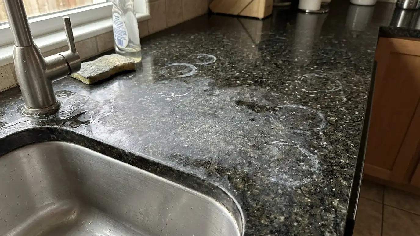 Before: a granite counter with a dull, cloudy surface with dark water stains and etched rings near the sink
